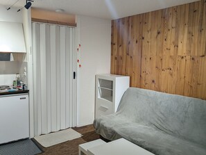 A compact living space with a kitchenette, a grey sofa, and a wooden panel wall. - Sunny studio for 4 with balcony, lake view, and WiFi (Besse-et-Saint-Anastaise-Super Besse)