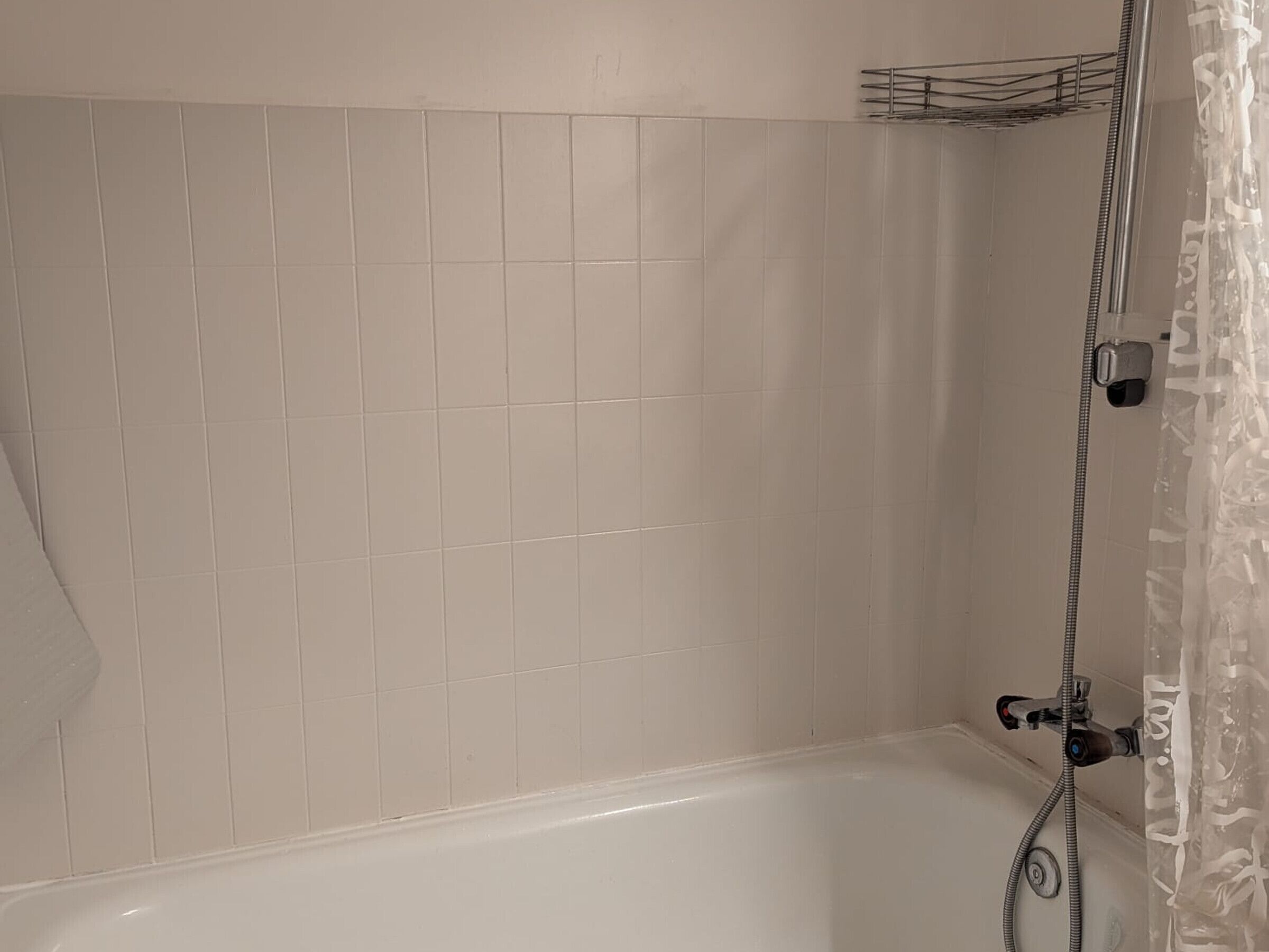 Ein Badezimmer mit weißen Fliesen, einer Badewanne und einer Dusche mit Duschschlauch.