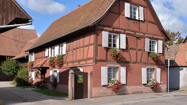 A traditional half-timbered building with a sloped roof, multiple windows with shutters, and flower boxes on the windowsills. - Charming Alsatian gîte near Colmar - 6 guests (Jebsheim)