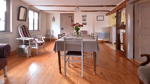 A dining area with a wooden table, chairs, and a vase of flowers. There are windows and a door in the background. - Charming Alsatian gîte near Colmar - 6 guests (Jebsheim)