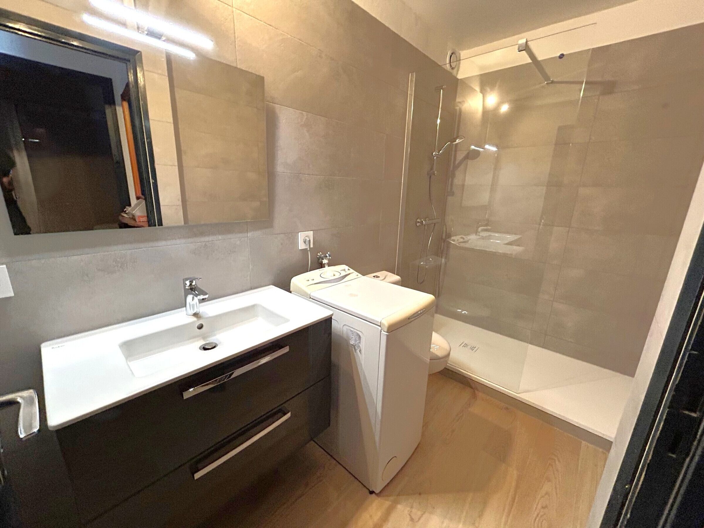 Une salle de bain moderne avec un grand miroir, un lavabo blanc, des toilettes blanches et une douche à parois de verre.