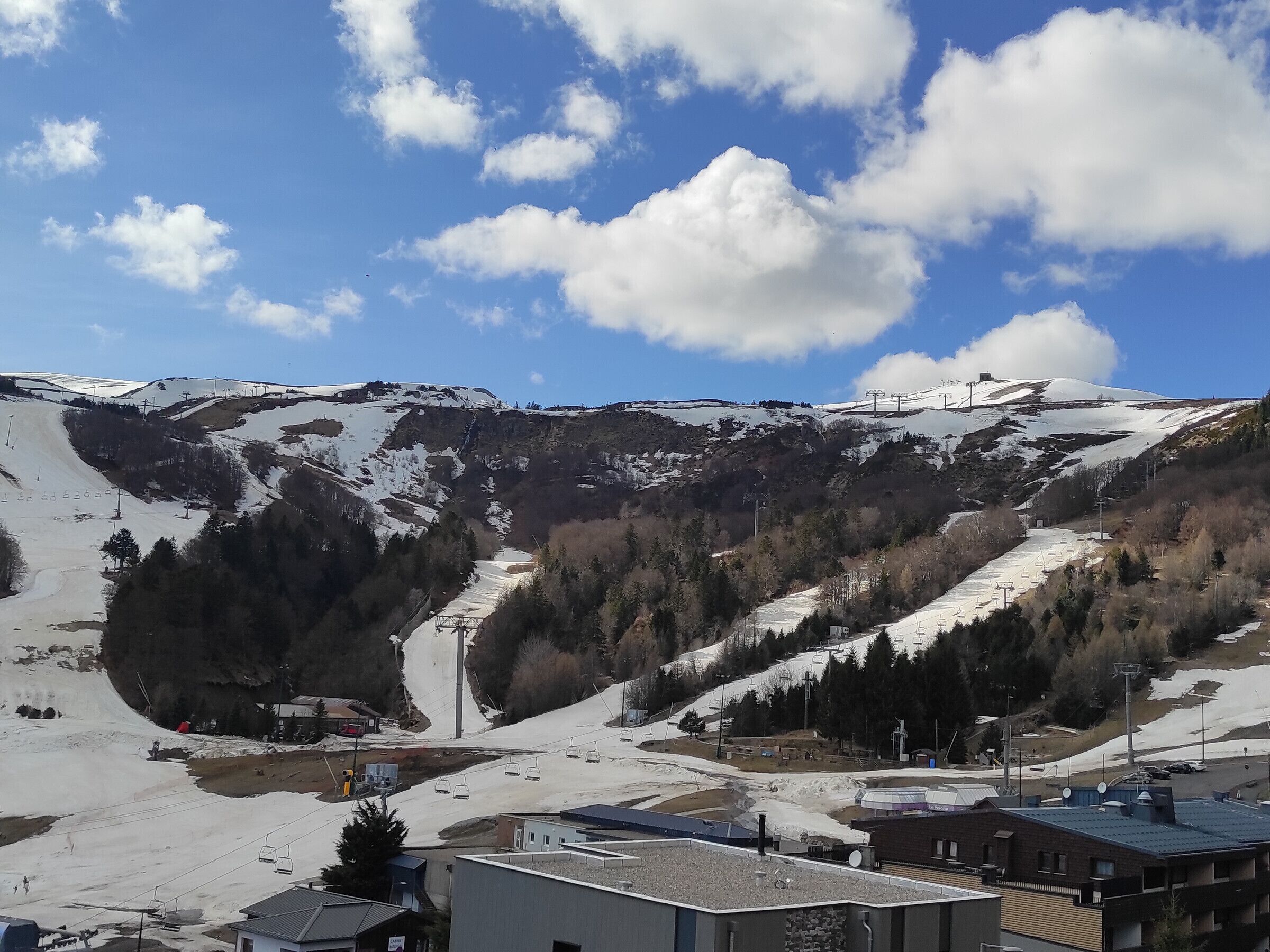 A mountainous landscape with a ski lift, buildings, and snow-covered slopes.