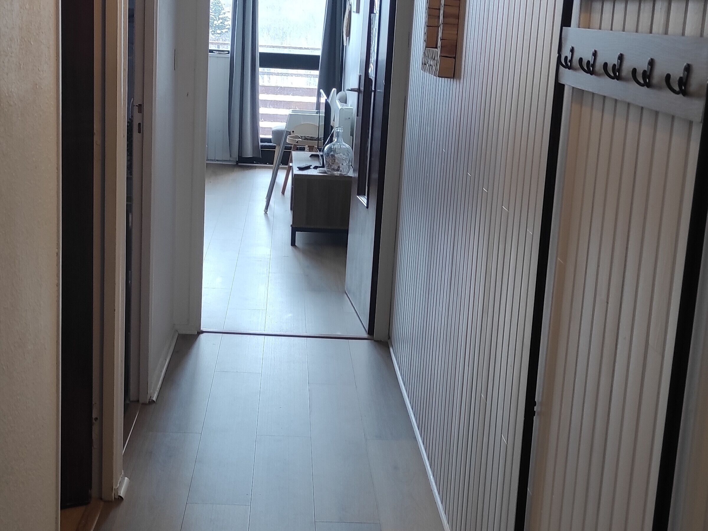A narrow hallway with a tiled floor leading to a room with a bed and a window.