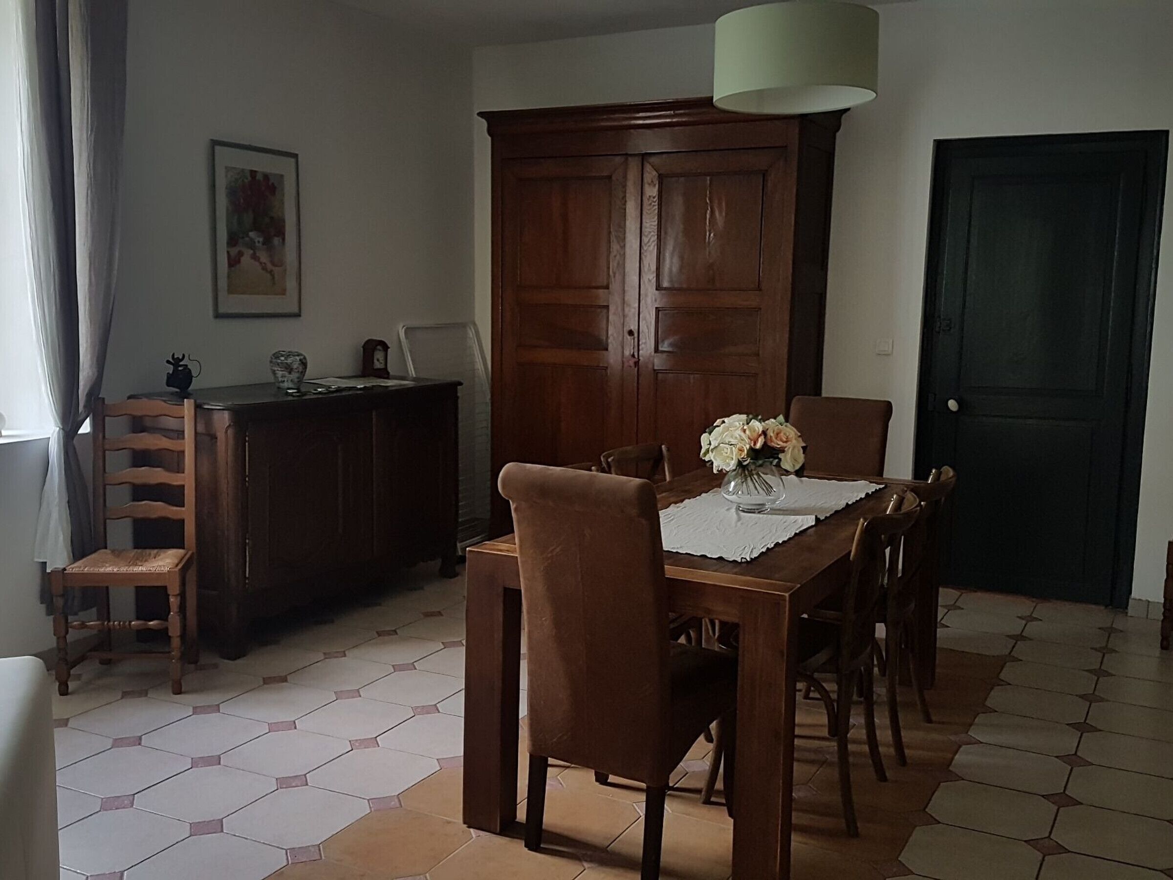 A dining area with a wooden table, chairs, a vase of flowers, a cabinet, and a door.