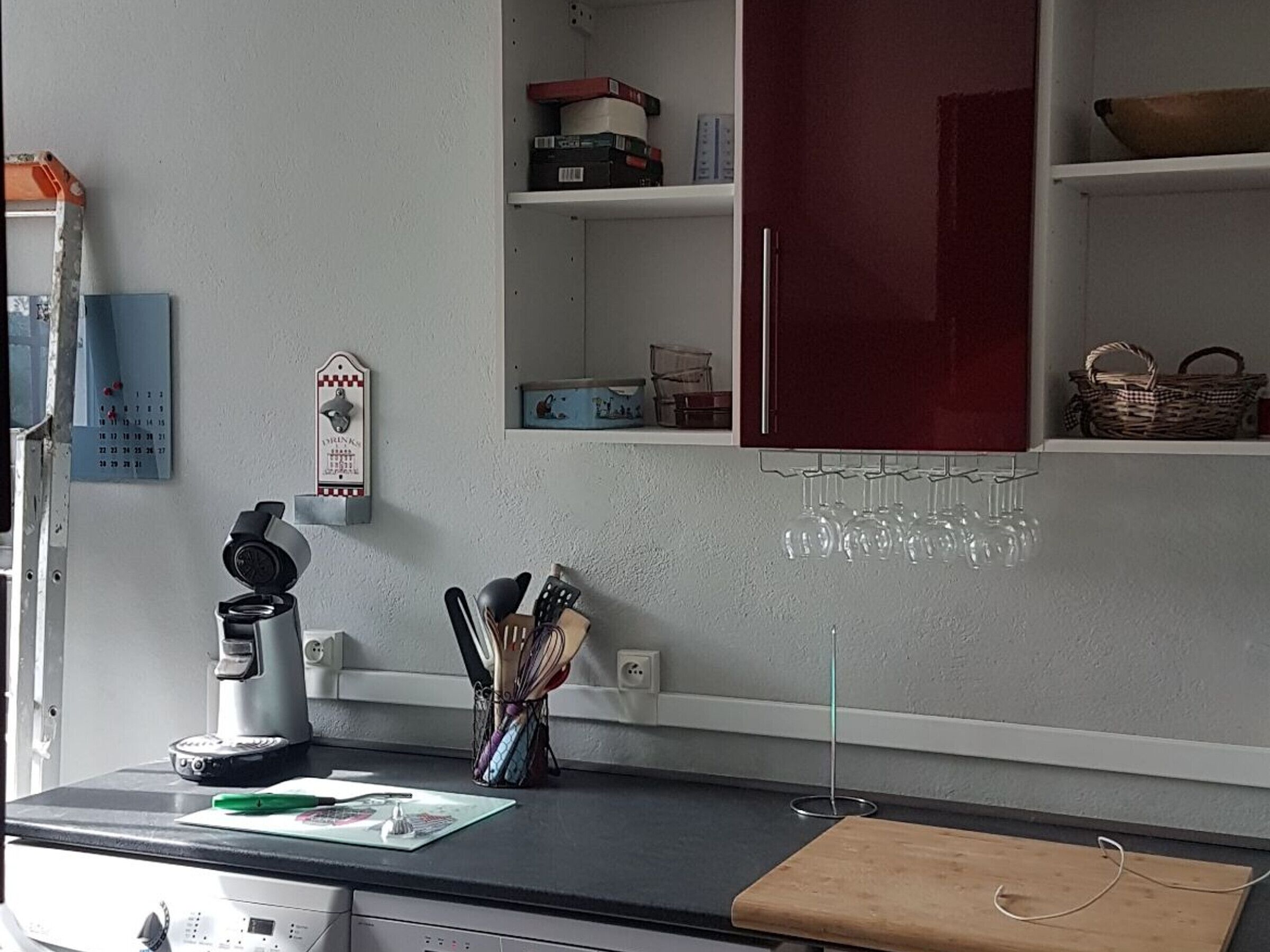 Une cuisine équipée d’une machine à café, d’ustensiles de cuisine, d’un calendrier et d’un porte-bouteilles.