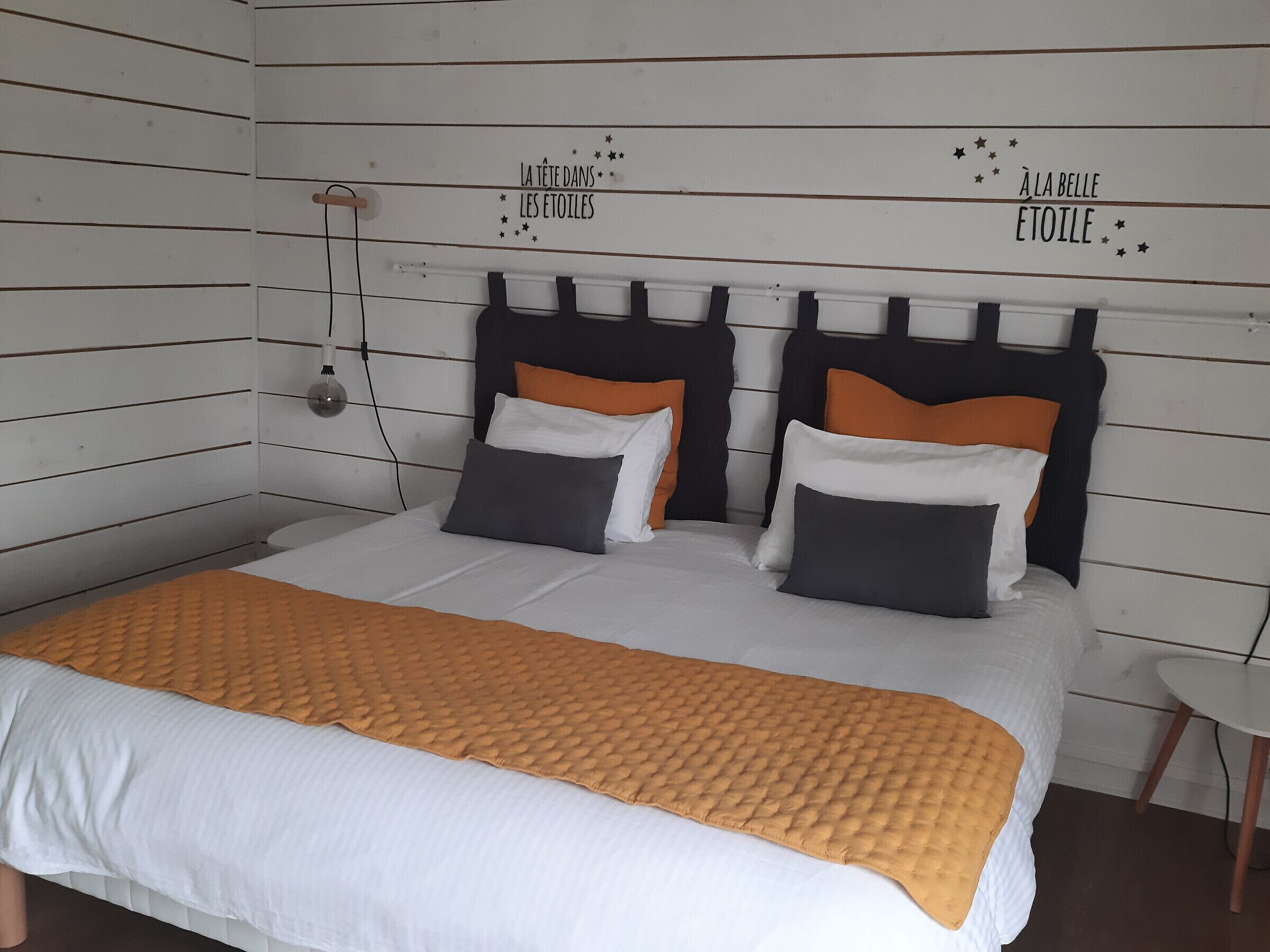 A bed with a white and orange bedspread, two pillows, and a headboard with text on the wall.