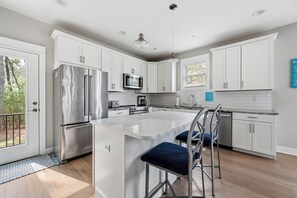 A modern kitchen with white cabinets, stainless steel appliances, and a central island with bar stools. - 4+BR, 3.5 BA  close to Bethany Beach & Town. 890B Garfield Parkway (Bethany Beach)
