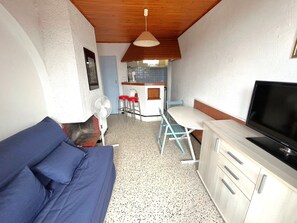 Un espace de vie compact comprenant un canapé, un téléviseur, une kitchenette et un ventilateur.