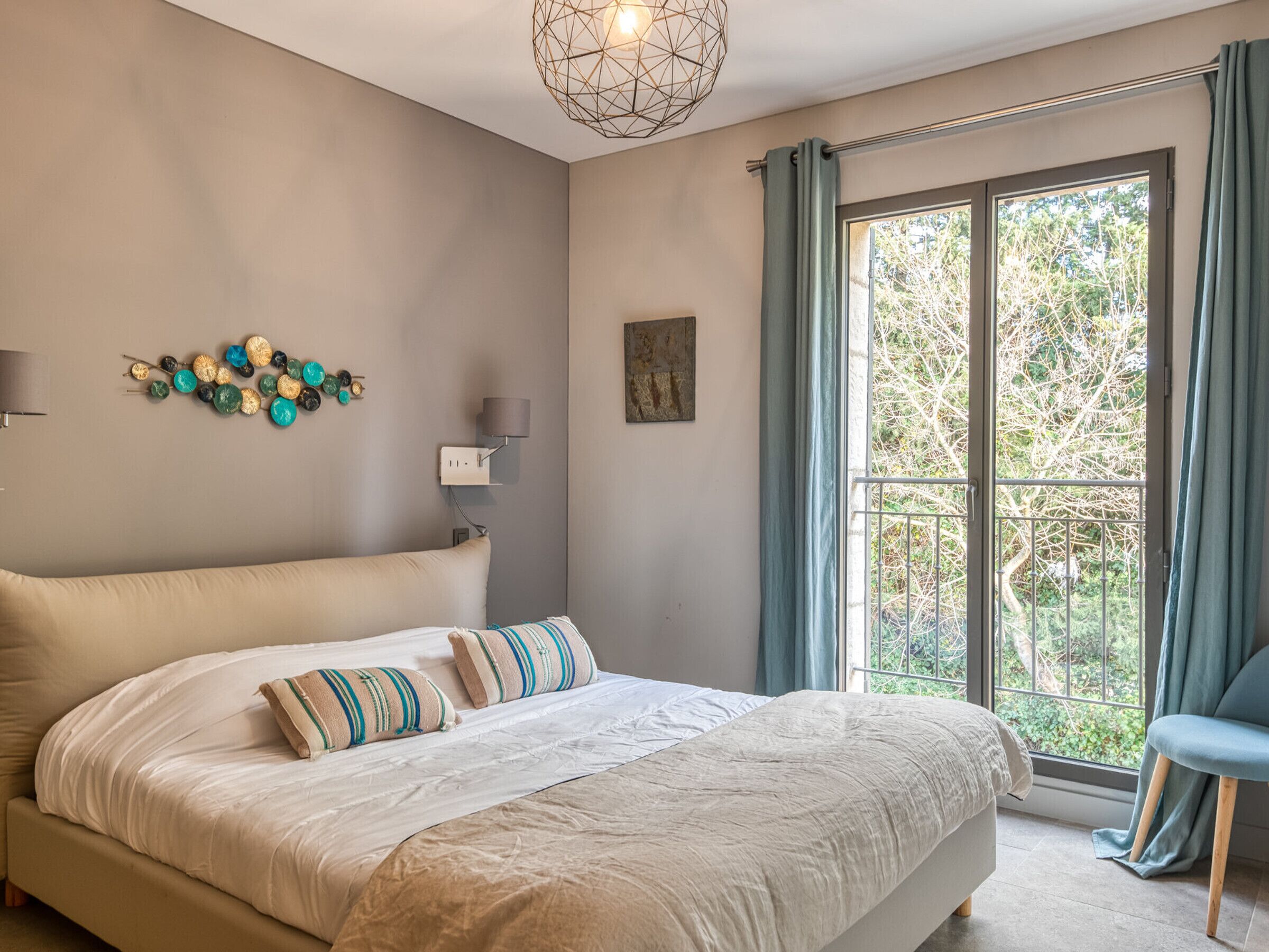 Un dormitorio con una cama grande, una lámpara de pared, un adorno en la pared y un ventanal con cortinas.