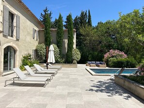 Zona de piscina amb gandules, una piscina i un edifici amb parets de pedra i persianes.