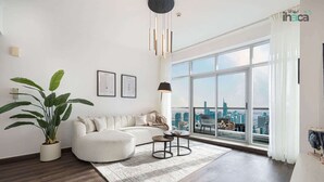 Ein modernes Wohnzimmer mit einem weißen Sofa, einer großen Kübelpflanze, einem runden Couchtisch und Blick auf eine Stadtlandschaft durch große Fenster.