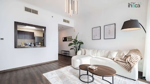 Ein modernes Wohnzimmer mit einem weißen Sofa, einem Couchtisch und einer großen Pflanze. Durch eine offene Tür ist eine Küche zu sehen.