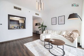 A modern living room with a white sofa, a coffee table, and a large plant. There is a kitchen visible through an open door. - 77 Floor Luxury 1Br Marina Sea View Balcony (Dubai)