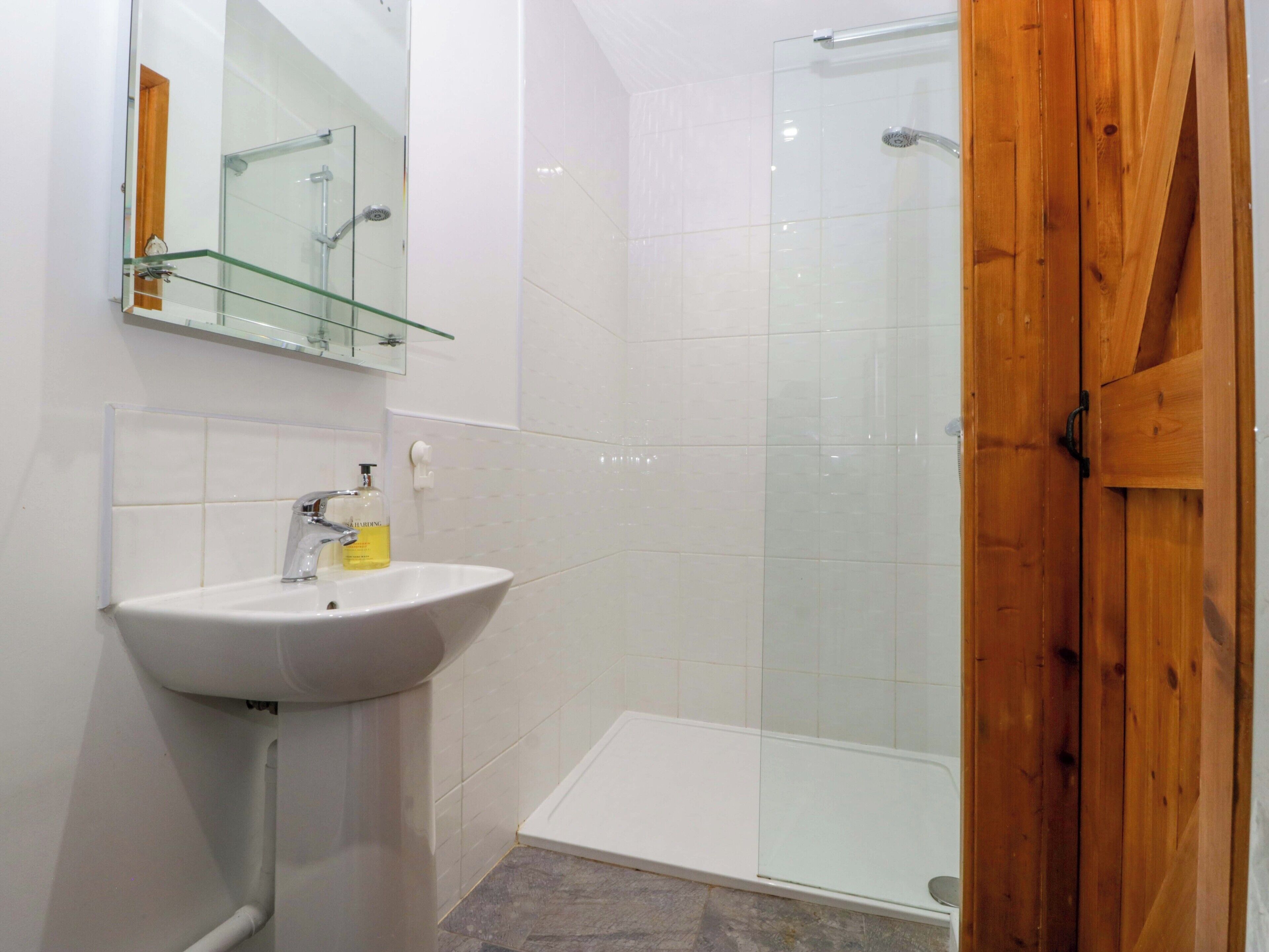Un baño con cabina de ducha de vidrio, un lavamanos blanco y una puerta de madera.