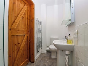 Ein Badezimmer mit Holztür, Toilette, Waschbecken mit Spiegel und Handtuchhalter.
