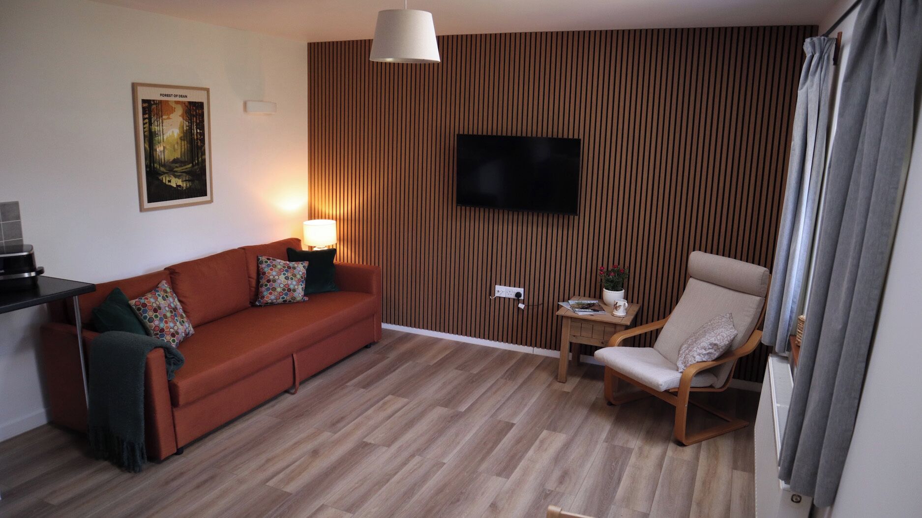 Un salon comprenant un canapé, un fauteuil, un téléviseur et une petite table avec une lampe.
