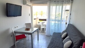 Un espacio habitable compacto con un sofá, una mesita, un televisor montado en la pared y una puerta corrediza de cristal que da a un área exterior.
