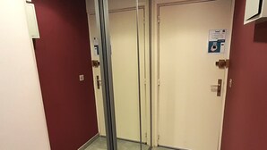 Un pasillo con un separador de vidrio, una puerta con un cartel y una pared roja.