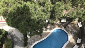 Vista aérea de una piscina rodeada de baldosas de piedra, con sillas de descanso blancas y un árbol grande cerca.