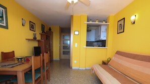 Una habitación compacta con cama, una mesa de comedor con sillas, kitchenette y ventilador de techo.
