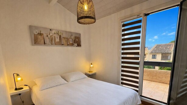Une chambre à coucher comprenant un lit, des lampes de chevet, une œuvre d’art accrochée au mur et une vue sur l’extérieur, accessible par une porte coulissante.