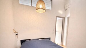 Une chambre à coucher avec un lit, un luminaire suspendu, une porte et une fenêtre.