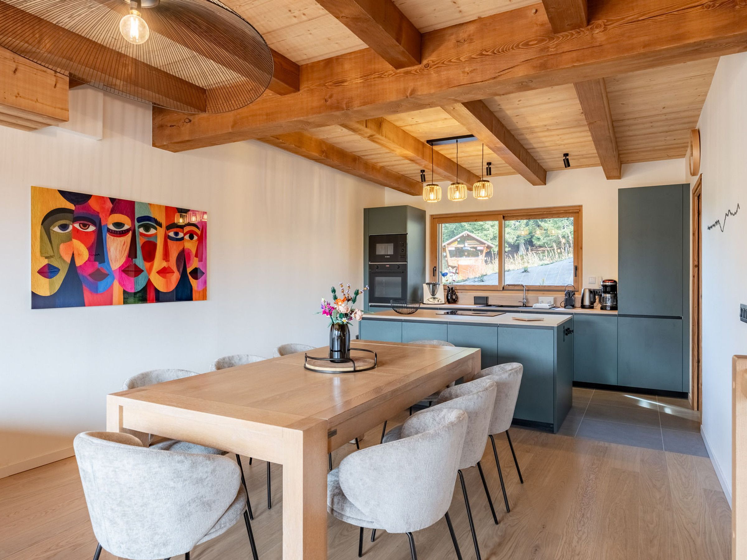 Une cuisine moderne avec un plafond en bois, un coin repas comprenant une table et des chaises, et une peinture abstraite aux couleurs vives accrochée au mur.