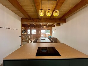 A modern kitchen with a central island, wooden ceiling beams, and pendant lighting. - 3-Bedroom Ski-In Chalet with Parking & Wifi (La Clusaz)