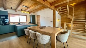 Eine moderne Küche mit einer Holzinsel, ein Essbereich mit Holztisch und Stühlen sowie eine Treppe mit Geländer aus Holz.