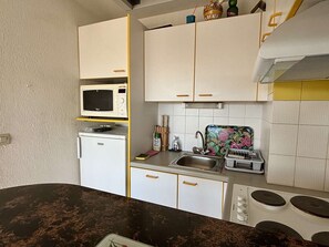 A compact kitchen with white cabinets, a microwave, a small refrigerator, a sink with a floral backsplash, and a stove. - Charming T2 in Argelès-sur-Mer with Air Con and Parking, near beaches (Argelès-sur-Mer)