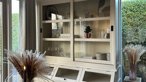 Ett vitt skåp med glasdörrar, som innehåller dekorativa föremål och en skylt med texten: ”Konstens olika uttryck – min livshistoria”.