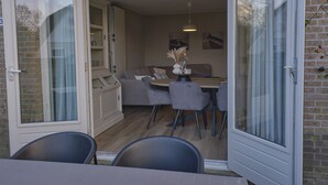 En öppningsbar skjutdörr leder in till ett matområde med ett bord, stolar och en soffa.