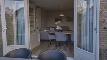 An open sliding door leading to a dining area with a table, chairs, and a sofa.