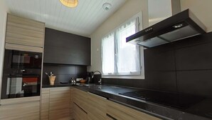 Une cuisine moderne avec des meubles de couleur sombre, un plan de travail noir et une fenêtre qui laisse entrer la lumière naturelle.