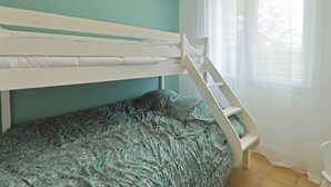 Un lit superposé avec une structure blanche et une couvre-lit à motifs verts.