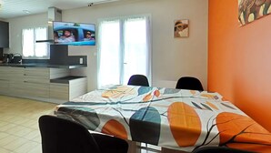 Un coin repas avec une table dressée pour quatre personnes, un téléviseur fixé au mur et une cuisine en arrière-plan.