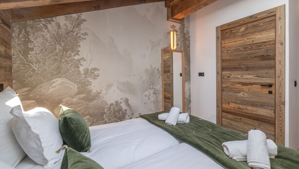 Een slaapkamer met een bed, kussens, een groene spreidek en een houten kledingkast.