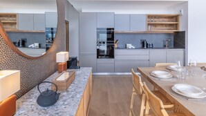 Een moderne keuken met grijze kastjes, een ingebouwde oven en een eethoek met een houten tafel voor vier personen.