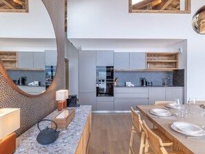 Eine moderne Küche mit grauen Schränken, einem eingebauten Ofen und einem Essbereich mit einem Holztisch, gedeckt für vier Personen.