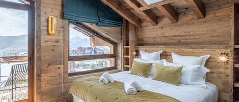 A wooden room with a bed, a window, and a view of a mountain.
