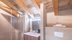 Een moderne badkamer met een douchecabine van glas, een houten plafond en een witte wastafel met spiegel.