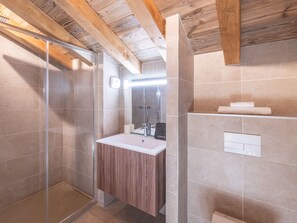 Ein modernes Badezimmer mit Duschkabine aus Glas, Holzboden und Waschbecken in Weiß mit Spiegel.
