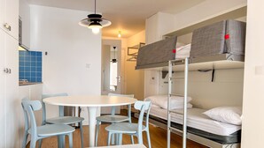A compact room with bunk beds, a round table with chairs, a hanging light fixture, and a blue-tiled backsplash in the kitchen area. - Renovated Studio 4 Pers Avoriaz, Mountain View (Avoriaz)