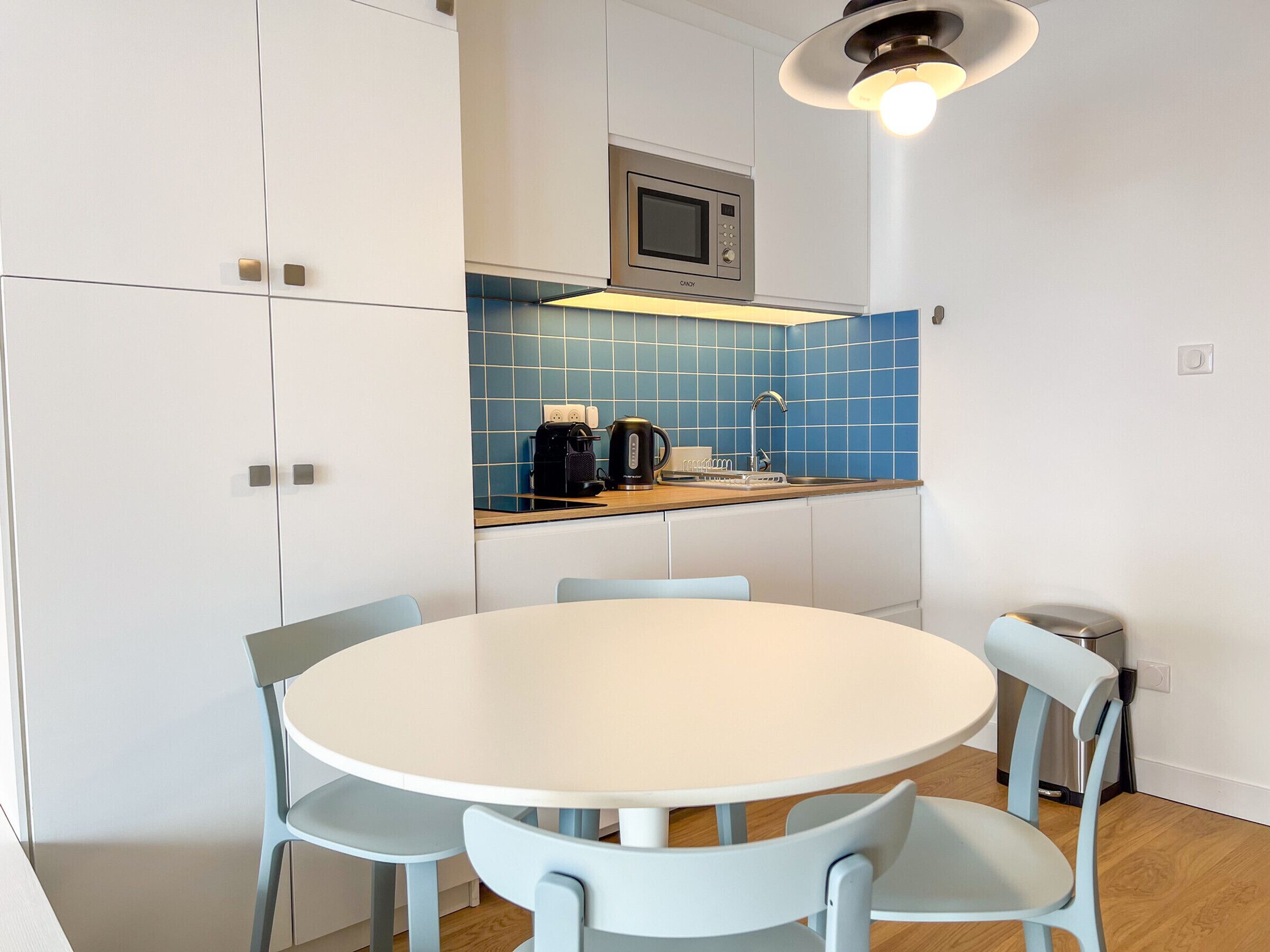 A compact kitchen with a microwave, coffee maker, and sink. There is a round table with four chairs.