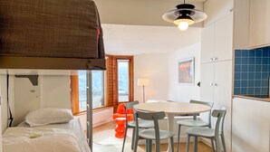 A compact hotel room with a bunk bed, a round dining table with chairs, a single lamp, and a view of the mountains through a window. - Renovated Studio 4 Pers Avoriaz, Mountain View (Avoriaz)