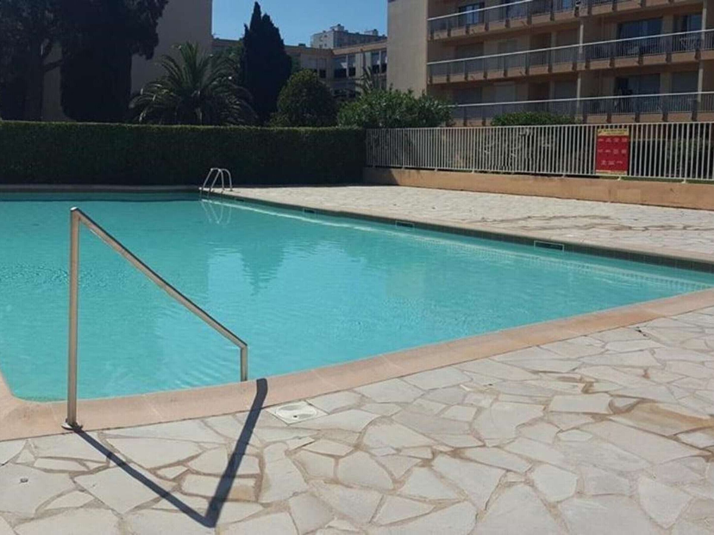 Piscina com escada de metal, rodeada por um deck de pedra.
