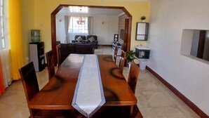 A dining area with a long wooden table, chairs, and a water dispenser. - Rhacky Homes Syokimau | Near JKIA 5 - 10 minutes' drive | Free WI-FI & Parking. (Machakos)