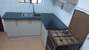 A compact kitchen with a gas stove, a sink, and beige cabinets. - Rhacky Homes Syokimau | Near JKIA 5 - 10 minutes' drive | Free WI-FI & Parking. (Machakos)