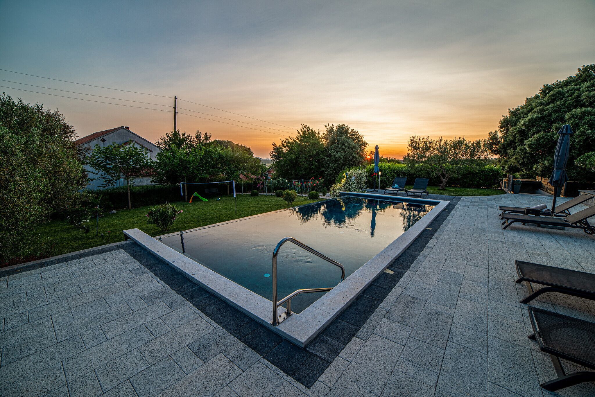 A rectangular swimming pool with a metal ladder, surrounded by a paved deck.