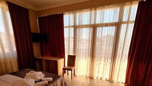 Una camera d'albergo con un letto, una sedia, una televisione e ampie finestre con tende.
